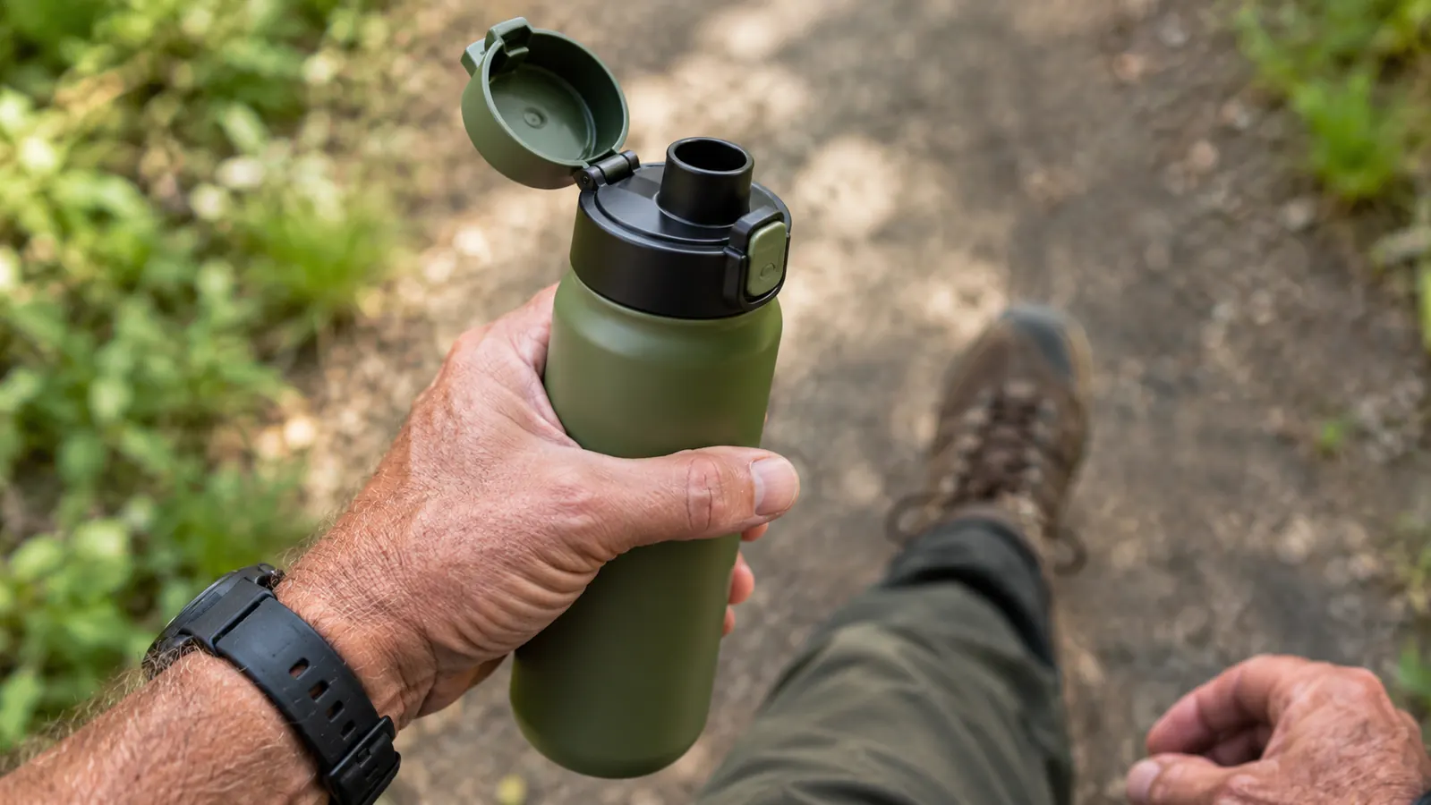 A hand holding a stainless steel water bottle with the spout open, ready to drink