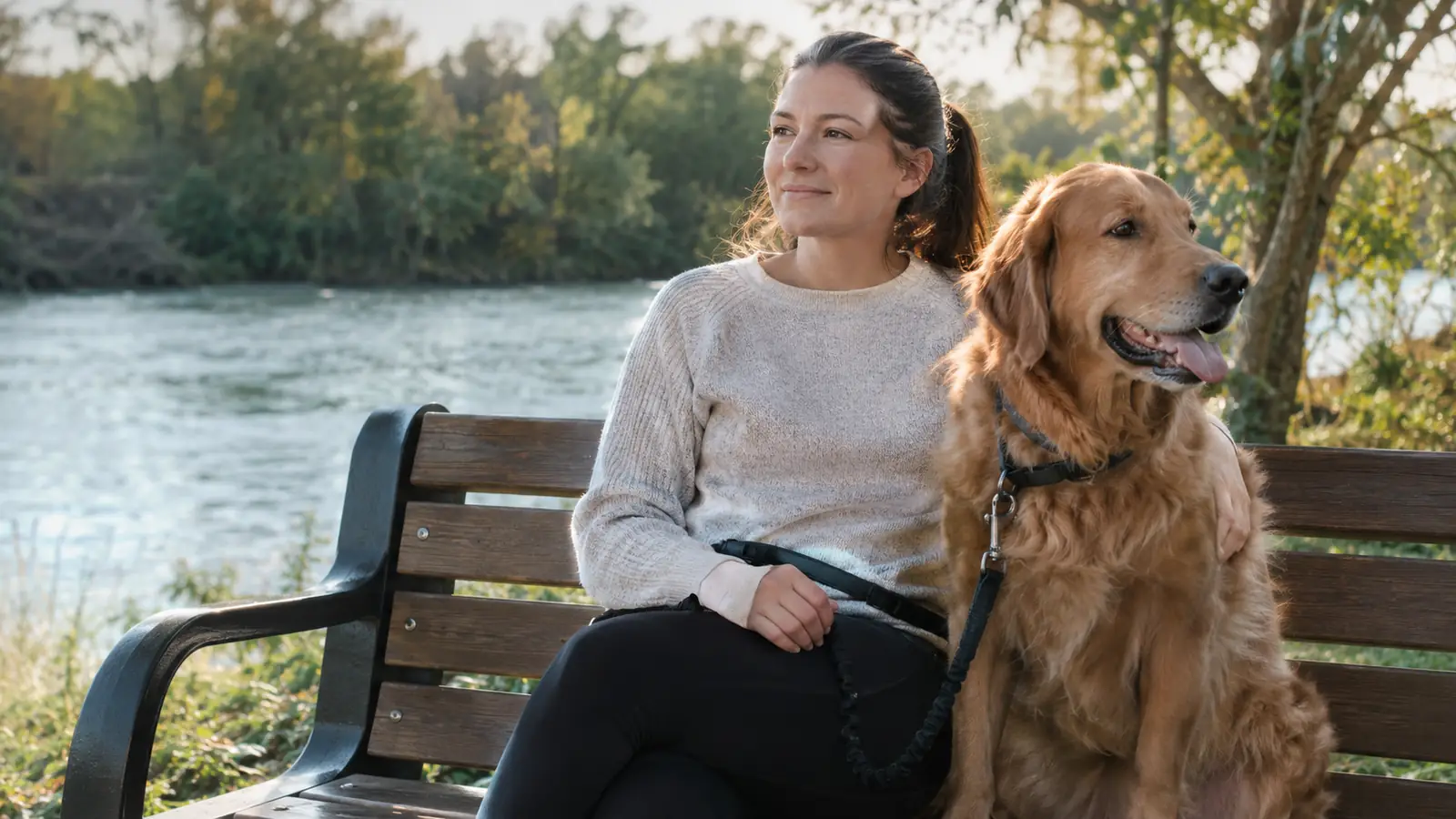A dog sitting beside a person on a park bench, the hands-free leash resting across the person's lap